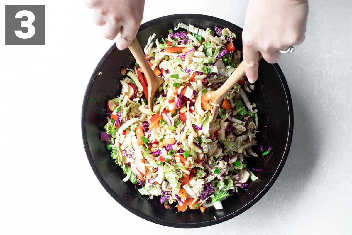 Top view of Napa Cabbage Salad being tossed in a black bowl with wooden salad spoons.
