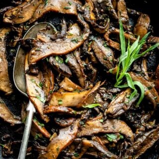 Top view of a close up of sautéed portobello mshrooms in a skillet with a spoon in it and fresh herb leaves on top.