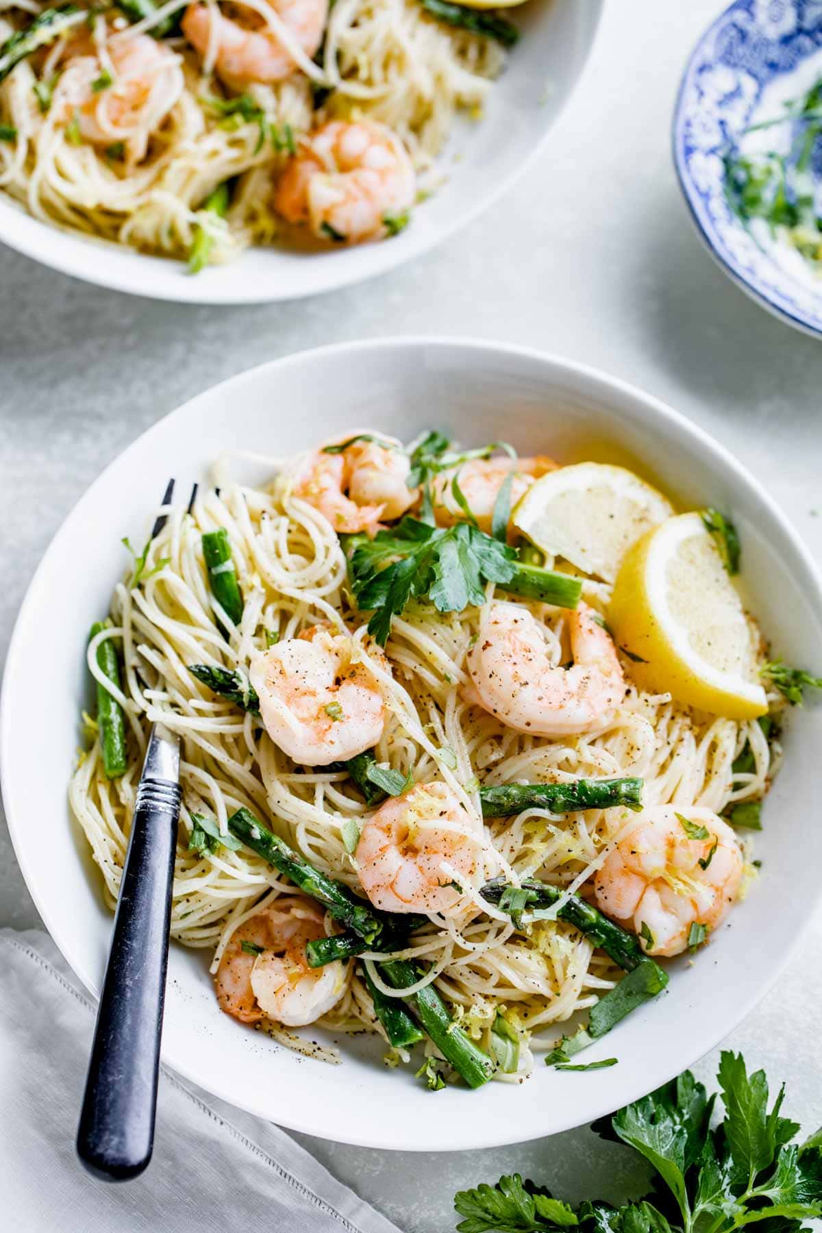 two bowls of shrimp and asparagus pasta on a white table with parsley