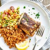 blackened cod fish fillet served on a white plate over a bed of rice and summer succotash
