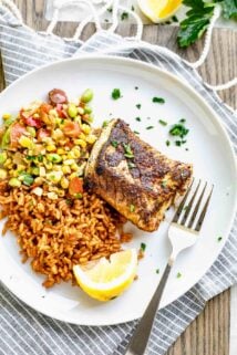 blackened cod fish fillet served on a white plate over a bed of rice and summer succotash