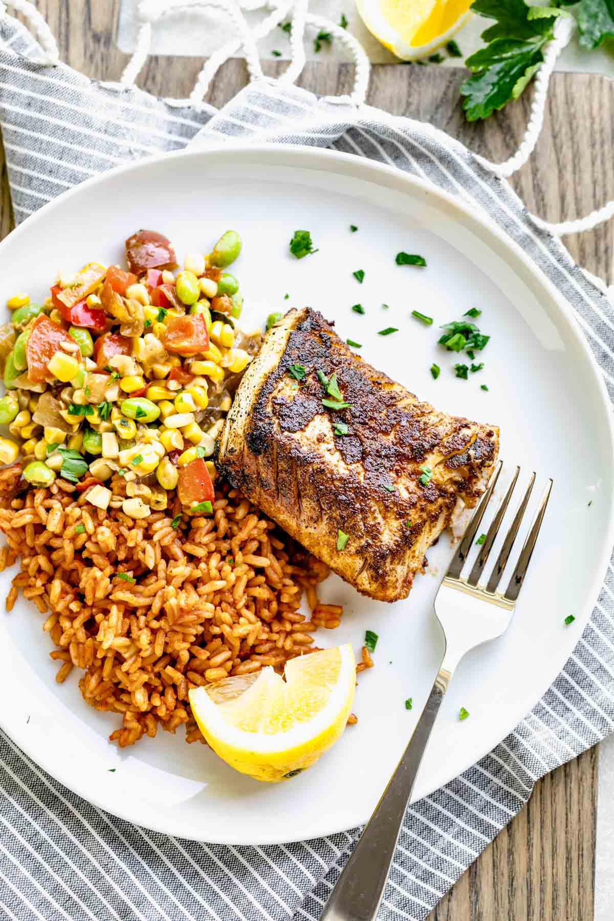 blackened cod fish fillet served on a white plate over a bed of rice and succotash 