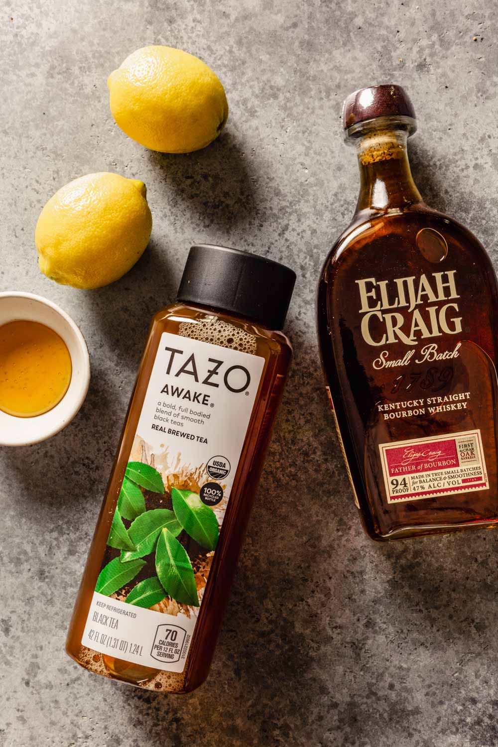 a bottle of bourbon and iced tea set on a counter with honey and lemons set around it