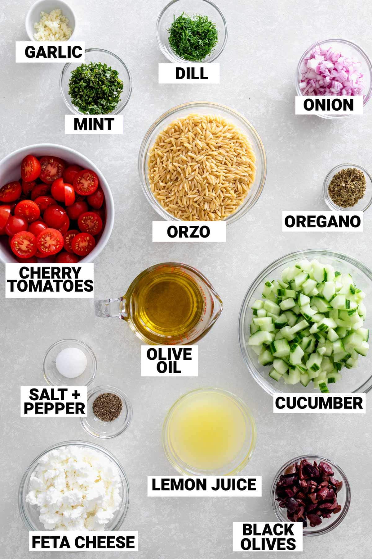 1 ½ cups dry orzo pasta (about 11 ounces) 1/3 cup lemon juice 1 clove garlic, finely minced ½ cup extra-virgin olive oil 2 tablespoons chopped fresh dill 2 tablespoons chopped fresh mint 2 ½ teaspoons dried oregano 1 ¼ teaspoon salt ½ teaspoon ground black pepper 1 pint cherry tomatoes, cut in half 1 European cucumber, peeled, seeded and diced 1 cup crumbled feta cheese, preferably reduced fat ½ cup pitted black Greek olives, roughly chopped ½ cup minced red onion in small glass bowls on a table.