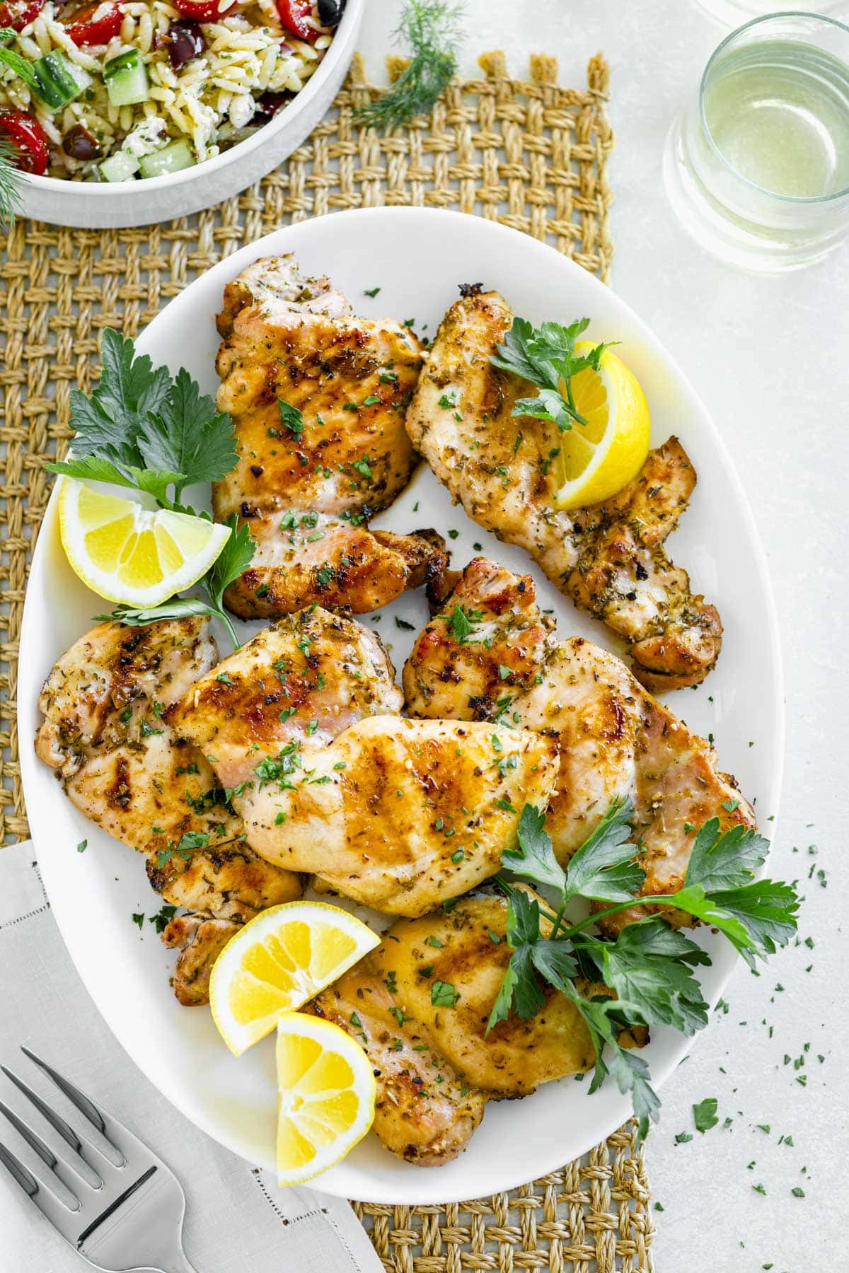 chicken thighs on a white platter with parsley and lemon