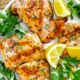 chicken thighs on a white platter with parsley and lemon