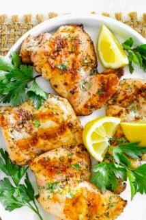 chicken thighs on a white platter with parsley and lemon