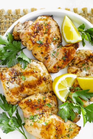 chicken thighs on a white platter with parsley and lemon