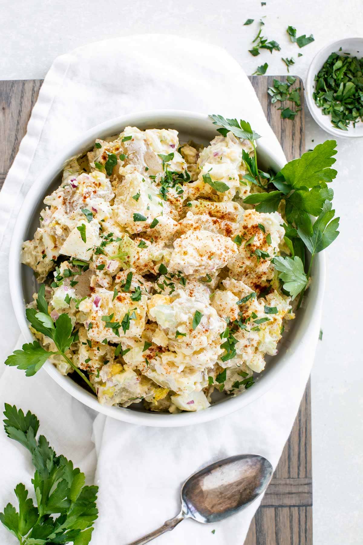 classic potato salad in a white modern bowl from overhead with a white napkin