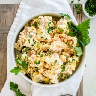 the potato salad in a modern white serving bowl with parsley leaves garnishing the side of the bowl