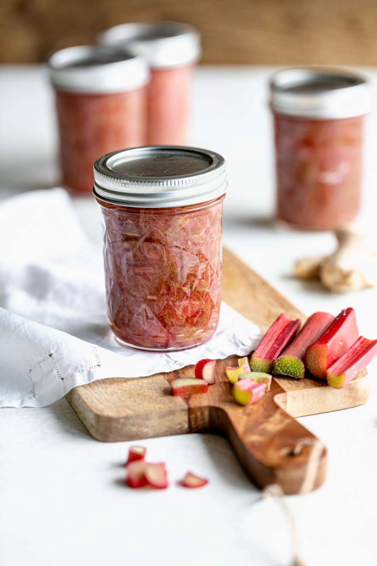 four jars of compote on a table with chopped rhubarb