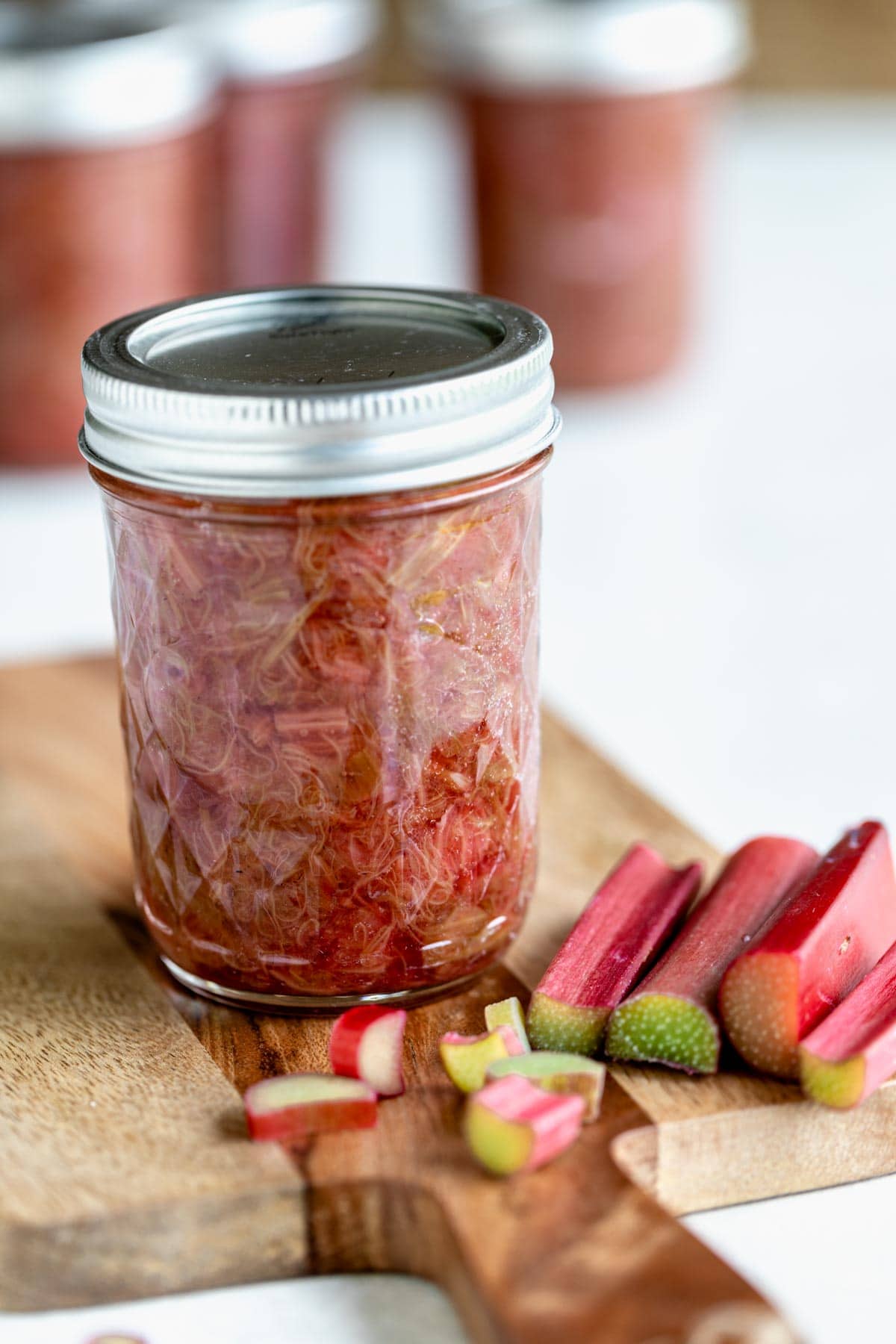 a jar of compote with chopped rhubarb on a wooden cutting board