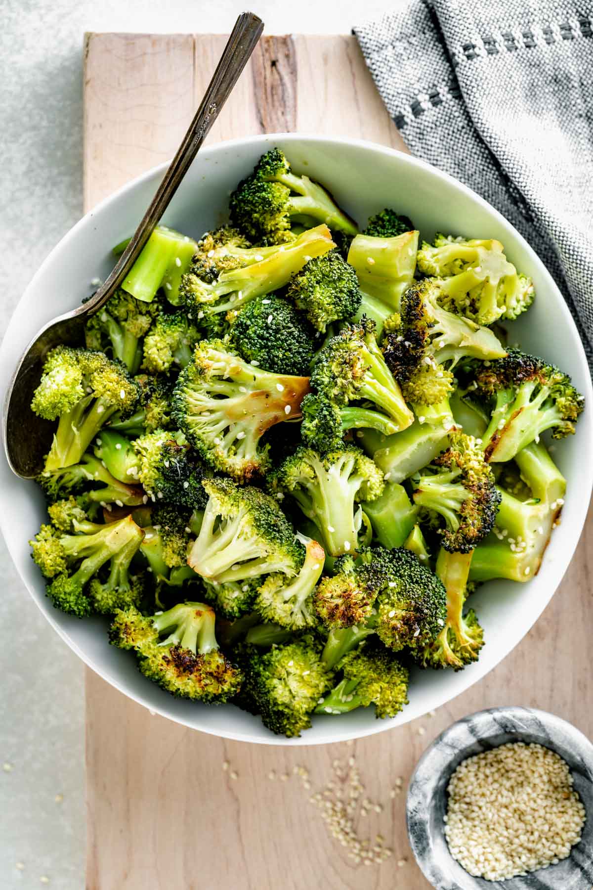 grilled broccoli in a bowl on a cutting board beside a small bowl of sesame seeds