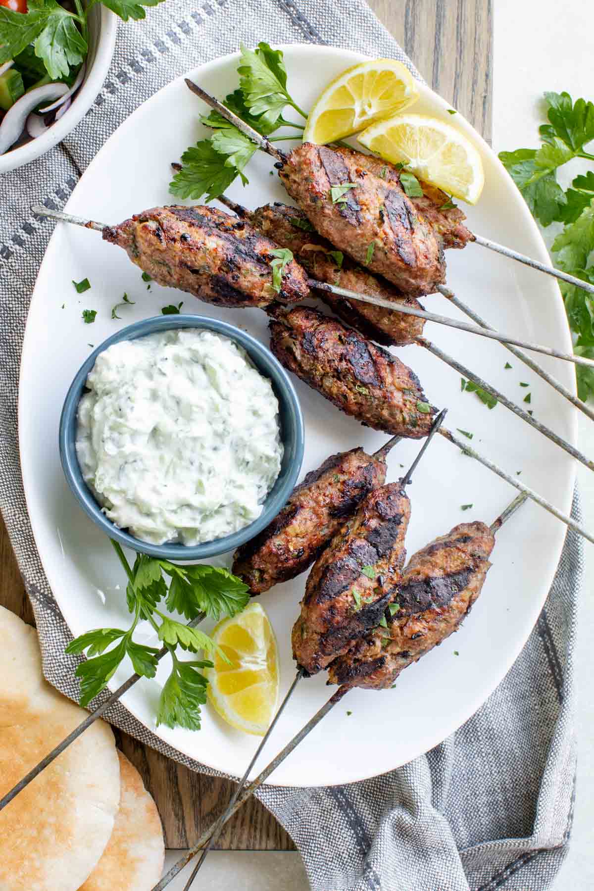 turkey kofta on skewers beside a bowl of greek yogurt cucumber sauce