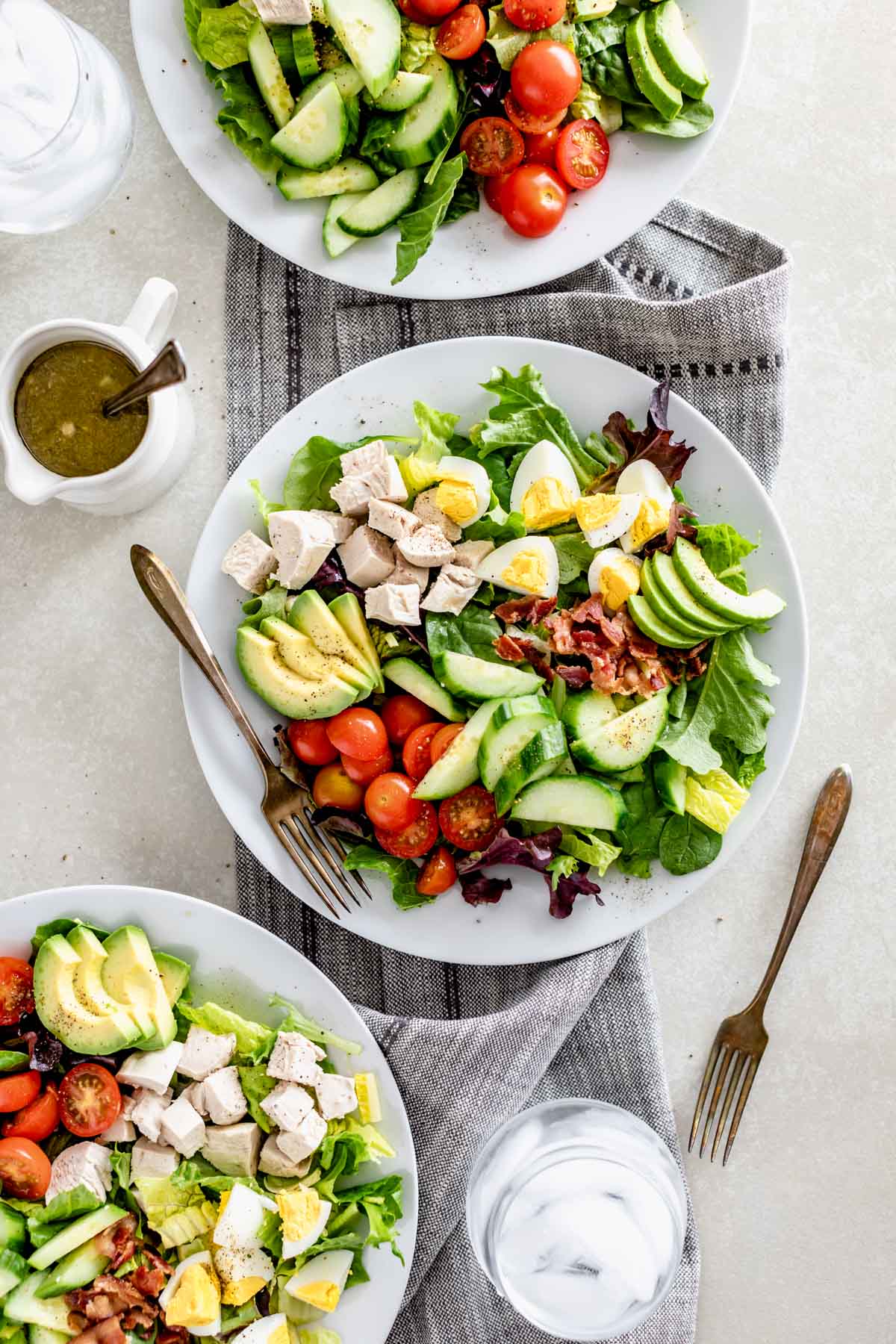 three healthy cobb salads on a table with ice water and a pitcher of the dressing