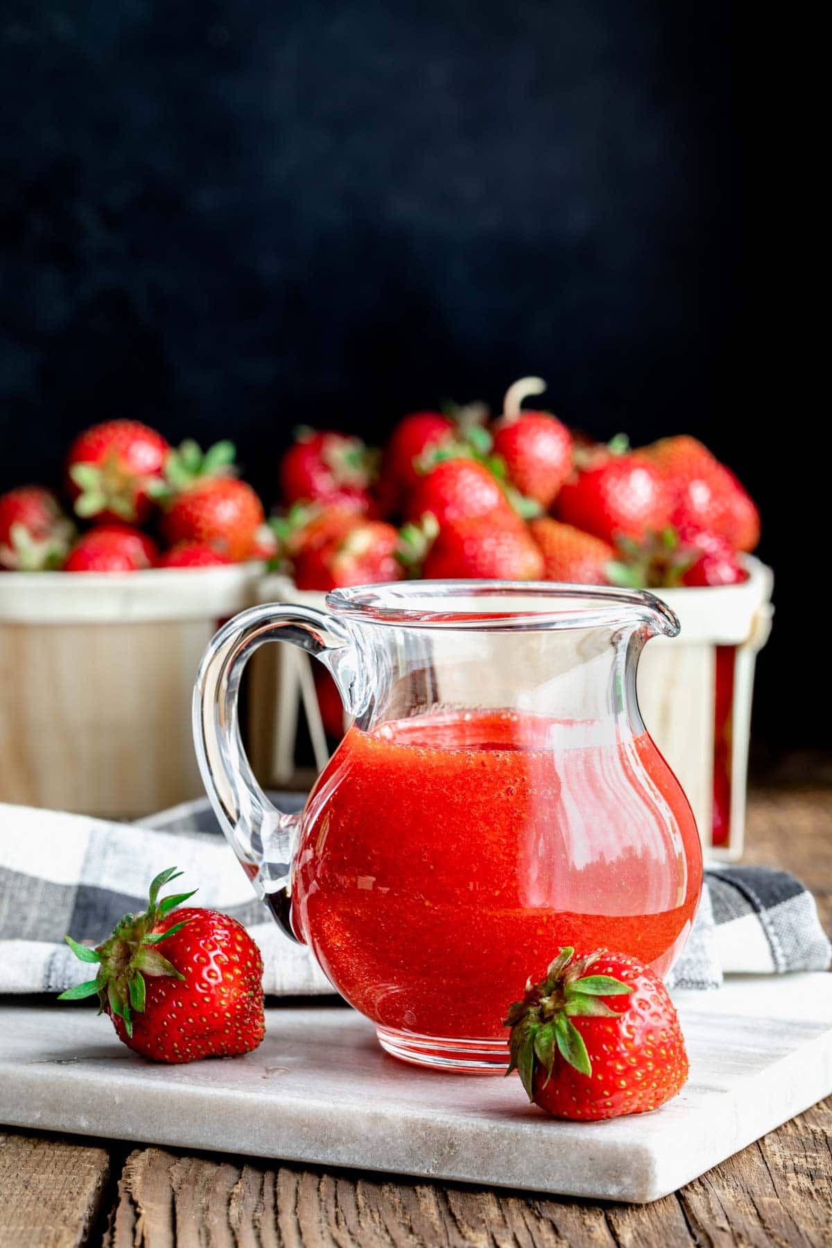 strawberry sauce in a small glass pitcher with quarts of strawberries
