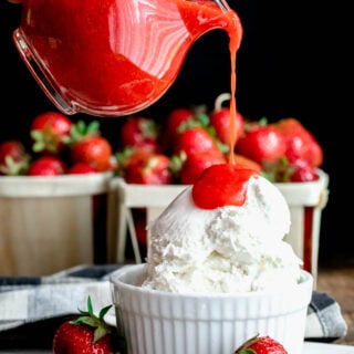 pouring strawberry coulis over ice cream with quarts of strawberries in the background
