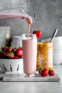pouring smoothie out of a blender into a glass with strawberries and peanut butter