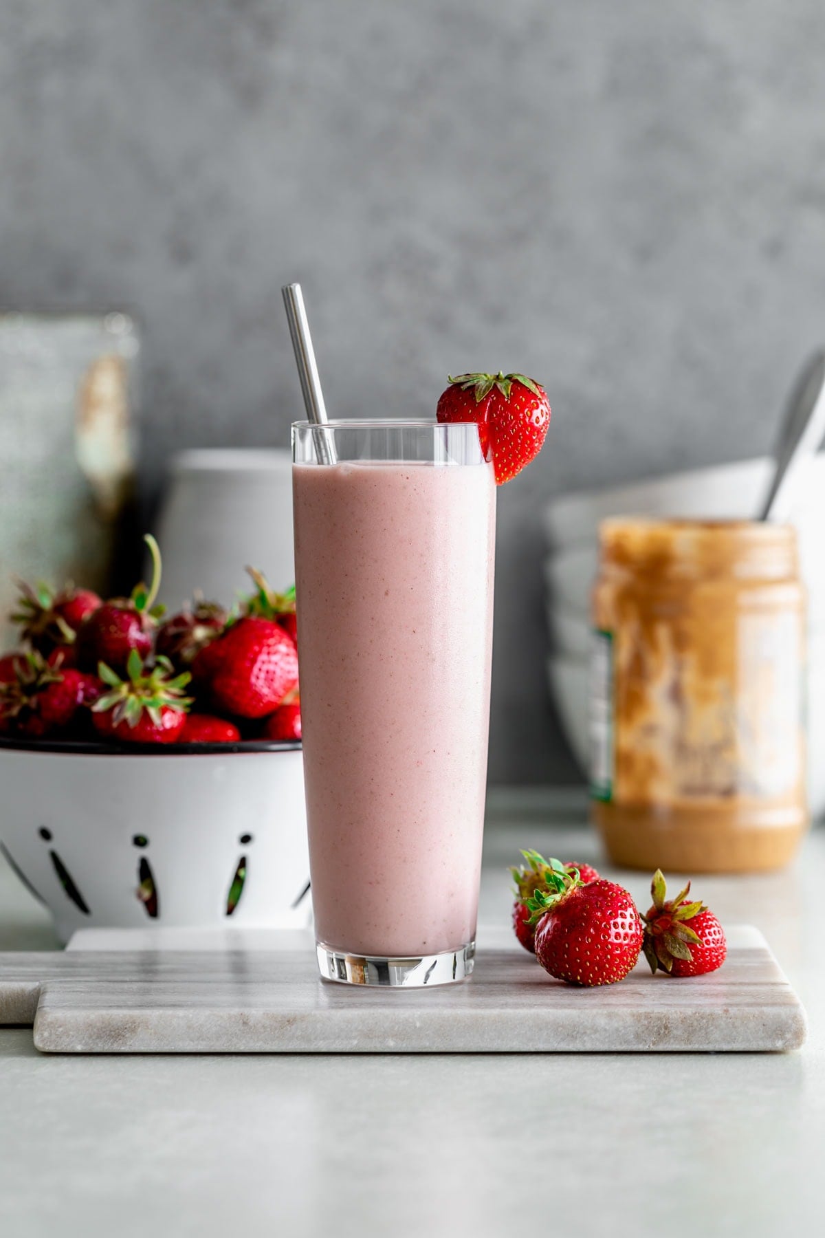 a smoothie with a metal straw and fresh strawberries with a jar of peanut butter in the background and berries