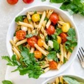 cherry tomato pasta in a white bowl with arugula on a white tabletop
