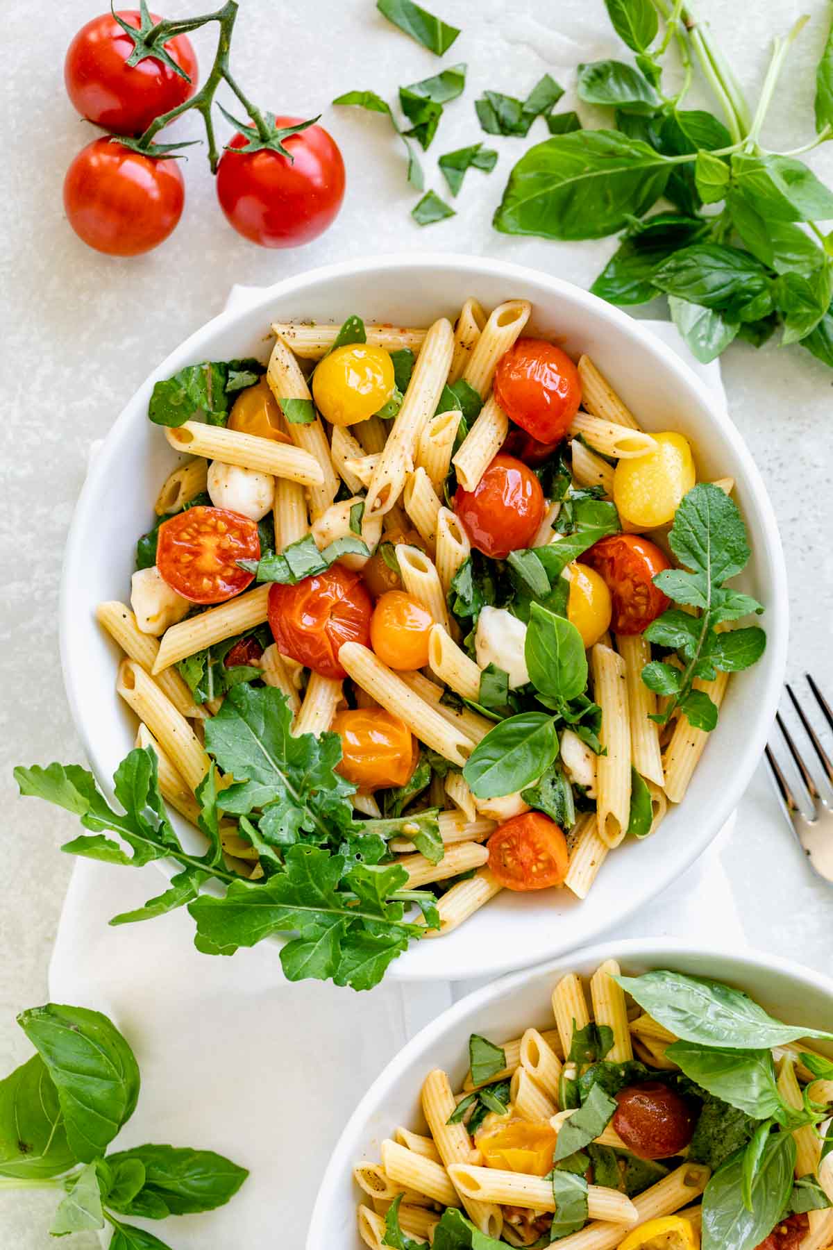cherry tomato penne caprese pasta in a bowl with arugula and basil