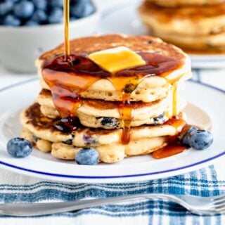 whole wheat blueberry pancakes with a pat of butter and syrup being poured on top