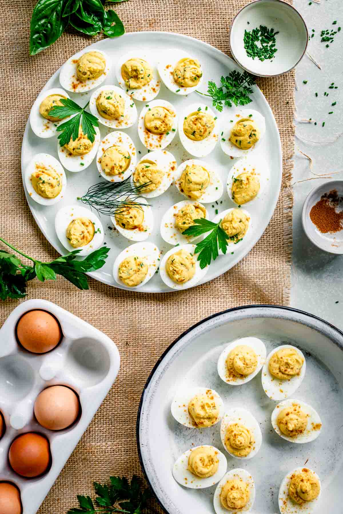 tablescape with two platters of deviled eggs, fresh herbs and a ceramic crate of whole brown eggs
