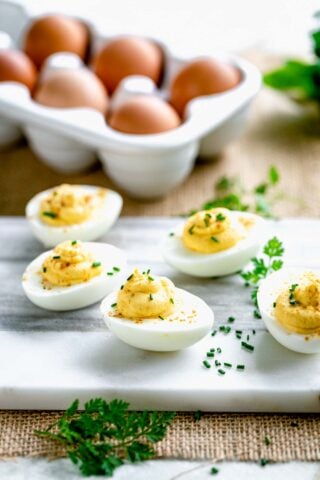 deviled eggs on a marble cutting board with a crate of eggs in the background