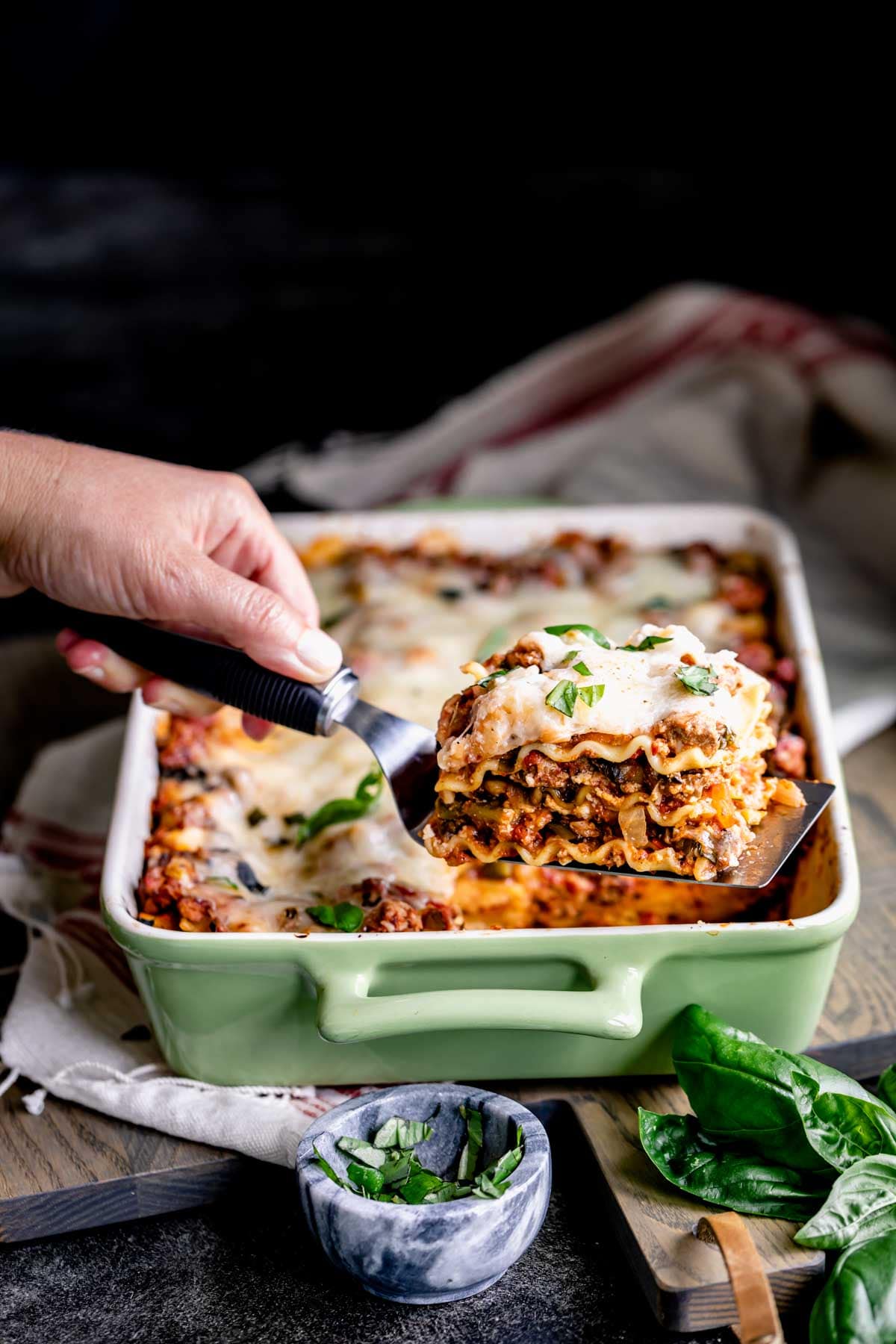 hand holding up a spatula with a slice of lasagna with the casserole dish in the background