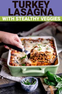 a hand holding a slice of lasagna on a spatula in front of a pan of lasagna