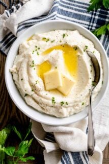 a white bowl with mashed cauliflower topped with melted butter