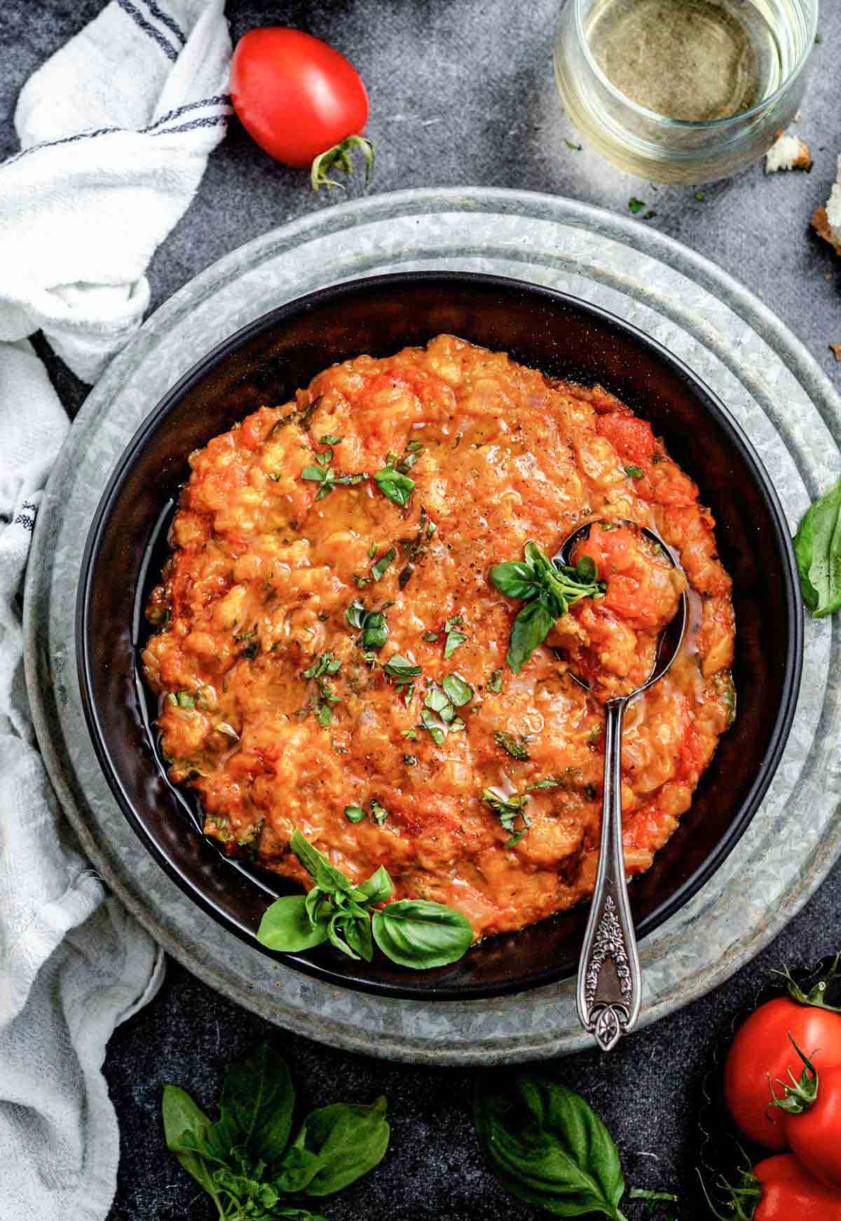 black bowl with thick tomato soup, garnished with basil sprigs and silver spoon
