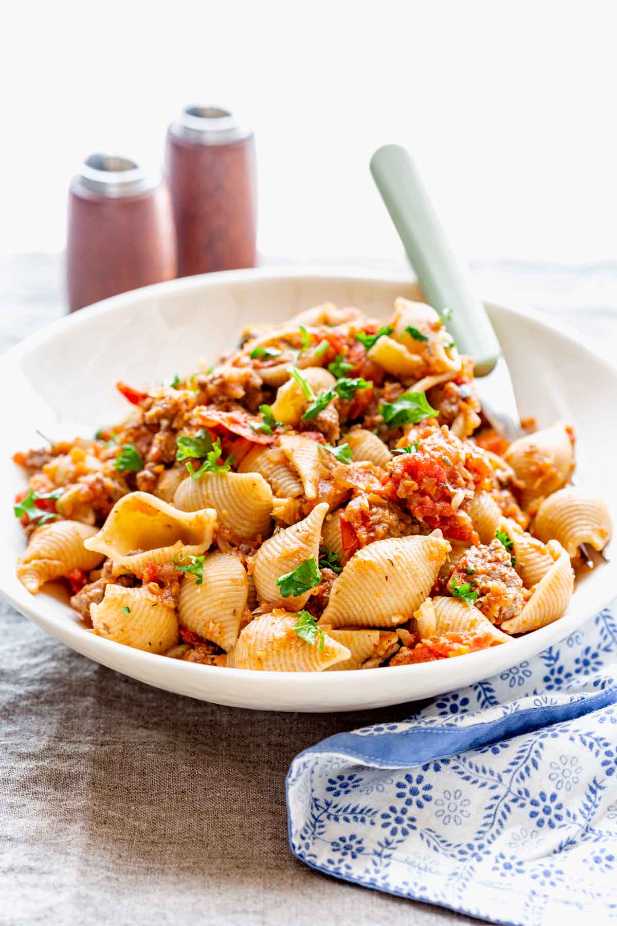 a white bowl with the chop suey in it with a fork and salt and pepper