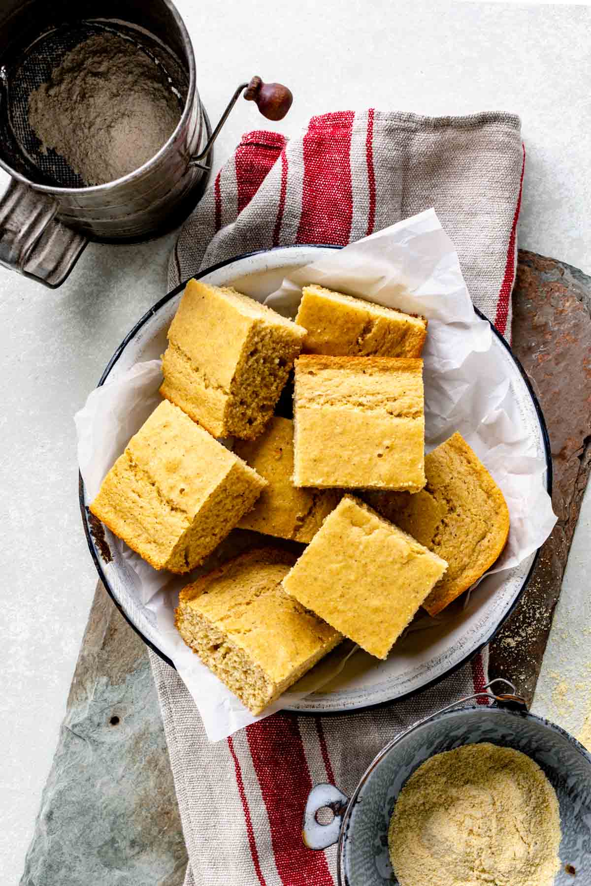 overhead of the cornbread with a sifter and bowl of cornmeal