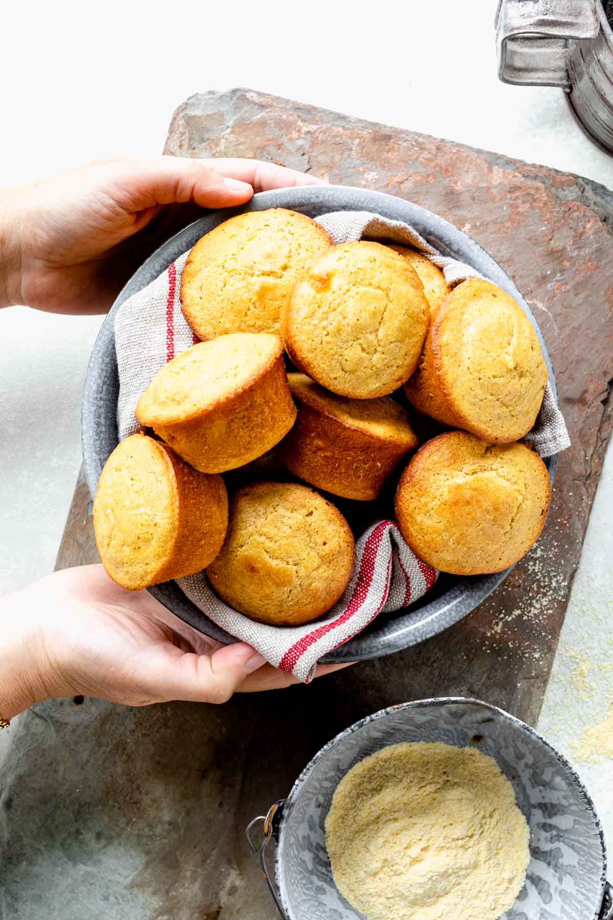 hands placing the metal bowl of muffins on the tabletop