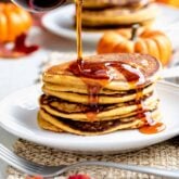 puring maple syrup over a tall stack of pumpkin pancakes with orange leaves in the foreground