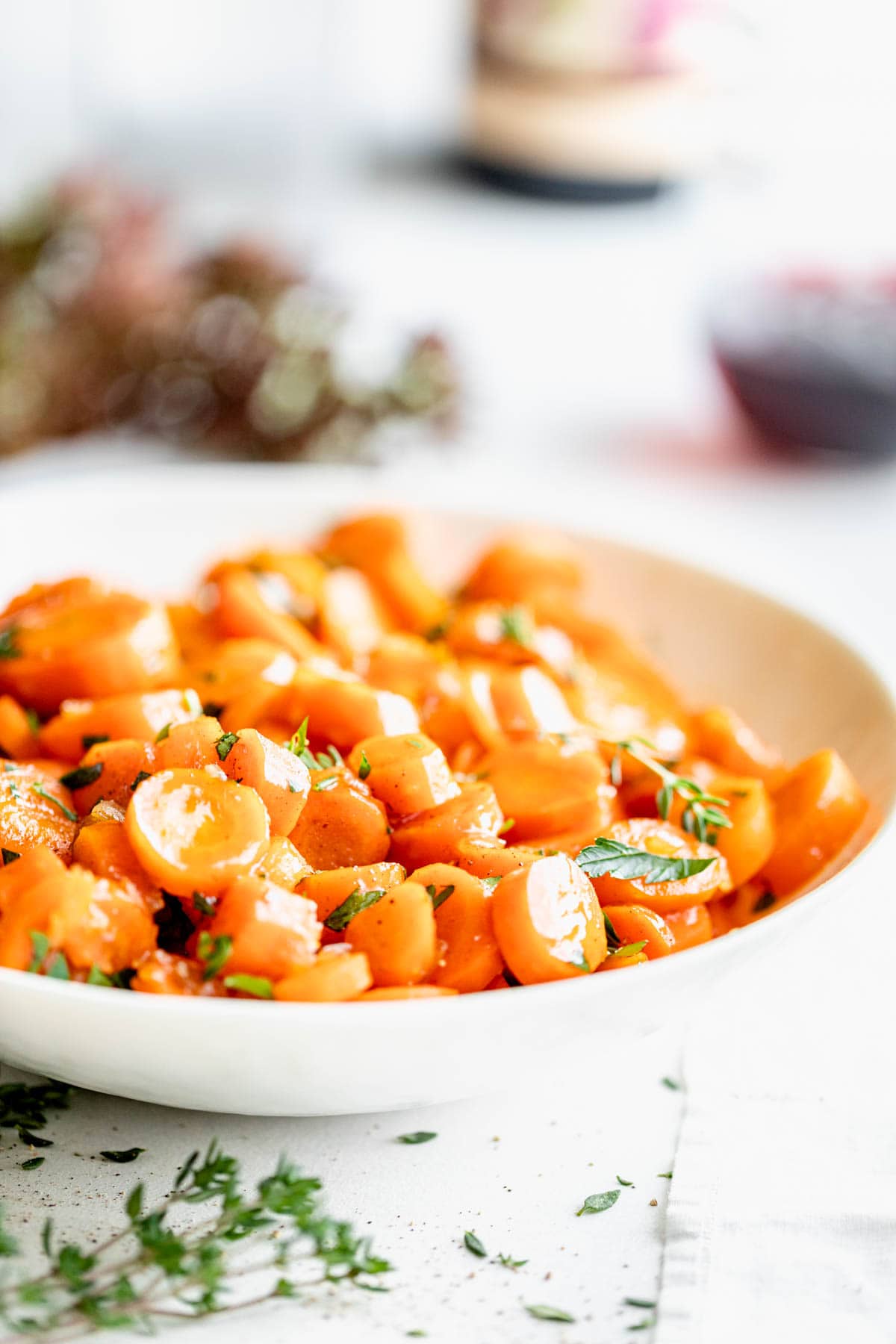 side view of the bowl of carrots with thyme sprigs in foreground and parsley on top