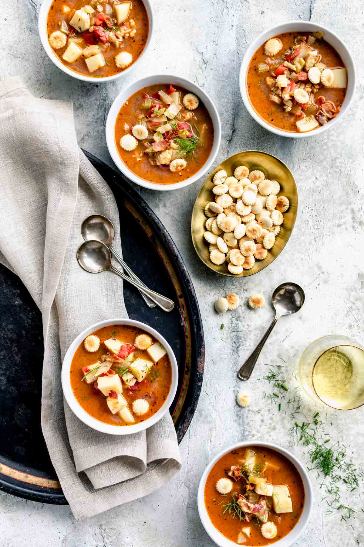 red clam chowder in bowls with oyster crackers and fennel scattered about with spoons