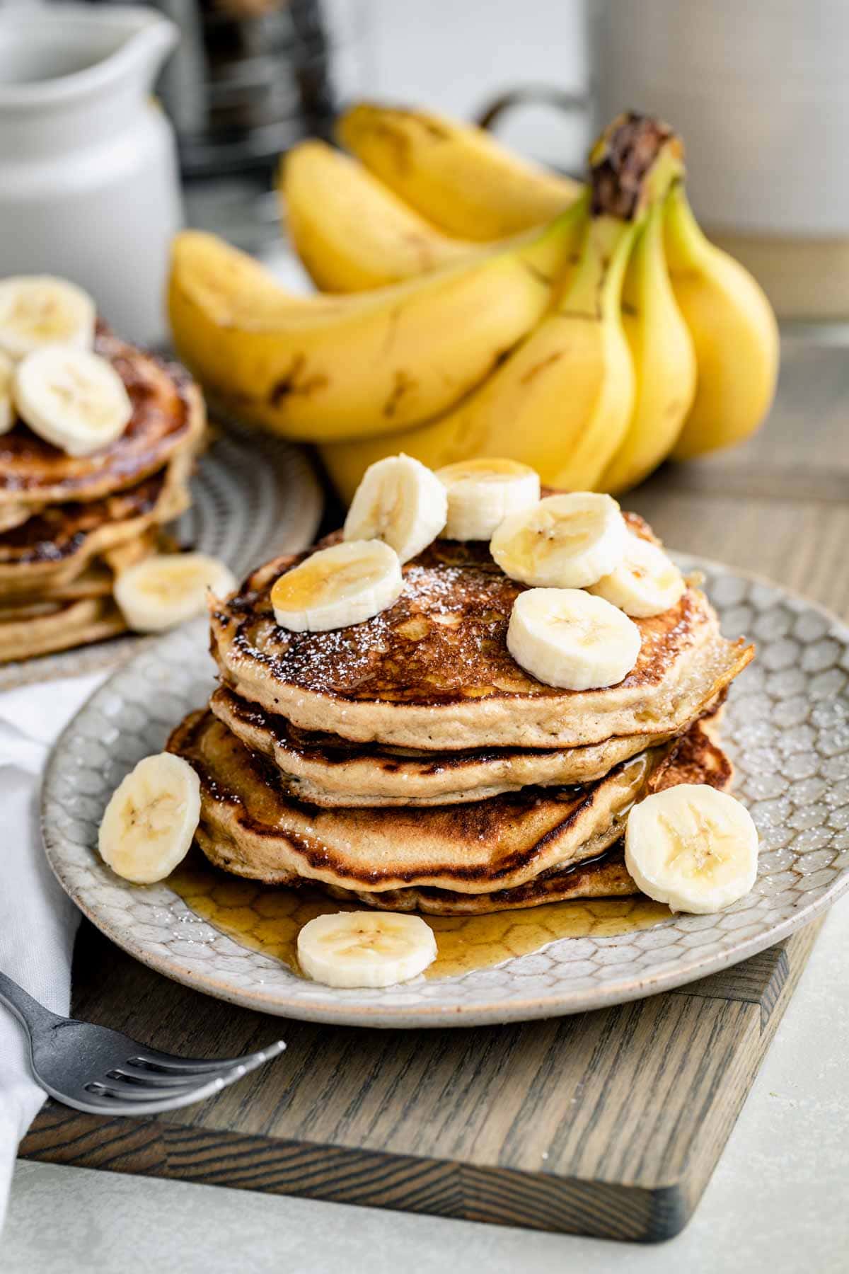 a stack of banana pancakes made with whole grain flour on a plate with slices of banana on top