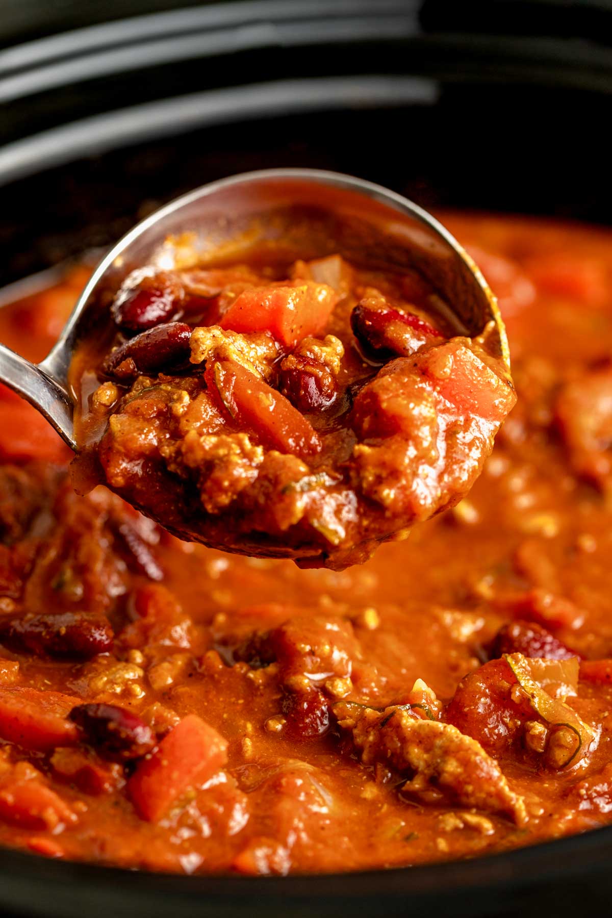 close up photo of a ladle full of turkey chili with a crockpot full in the background