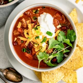 crockpot ground turkey chili in a bowl with cheese, greek yogurt, and tortilla chips on the side