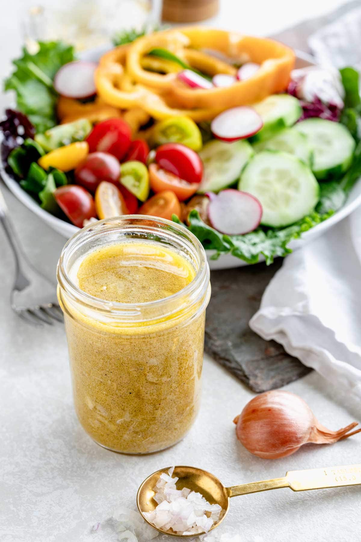overhead photo of vinaigrette in mason jar with salad behind