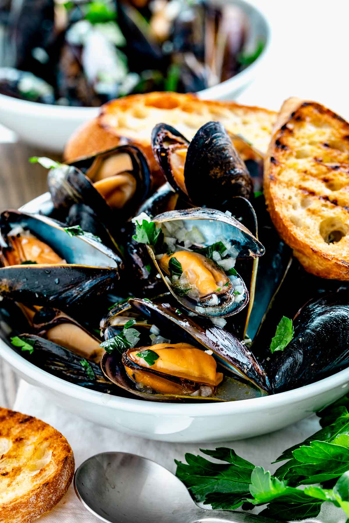 side angle of the mussels in a white bowl with grilled baguette
