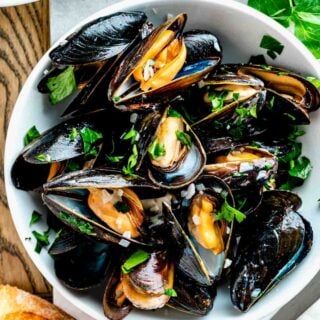 close-up of the steamed mussels in a white bowl with parsley on top