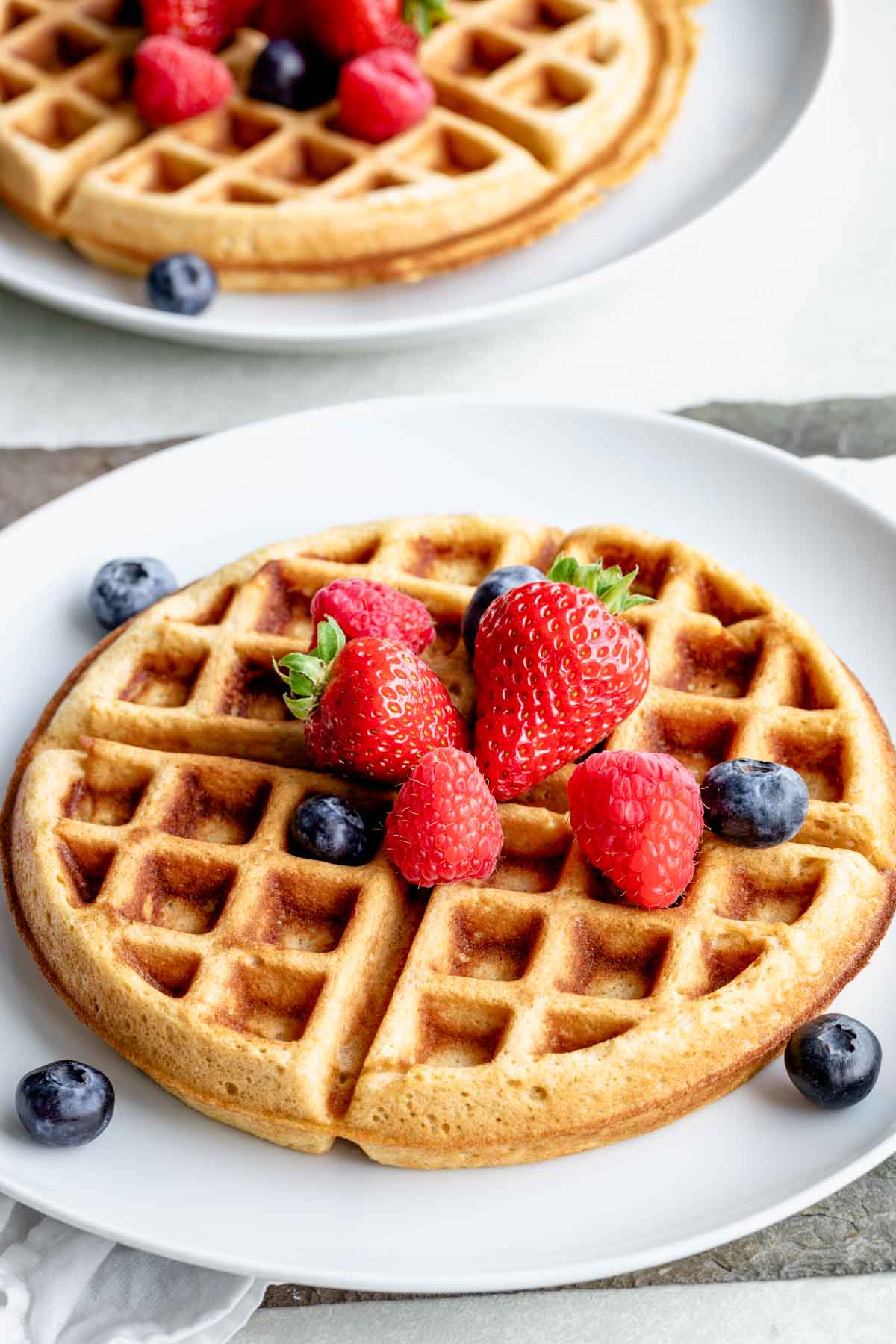 overhead view of whole wheat yeast waffles topped with fresh berries on white plate