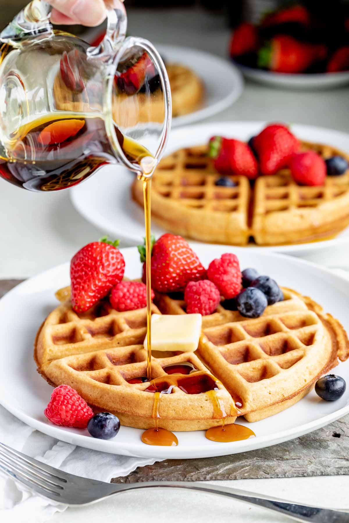 whole wheat yeast waffles topped with berries on a white plate with syrup being poured over