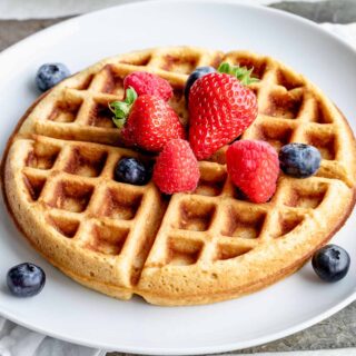 whole wheat yeast waffles topped with fresh berries on white plate.