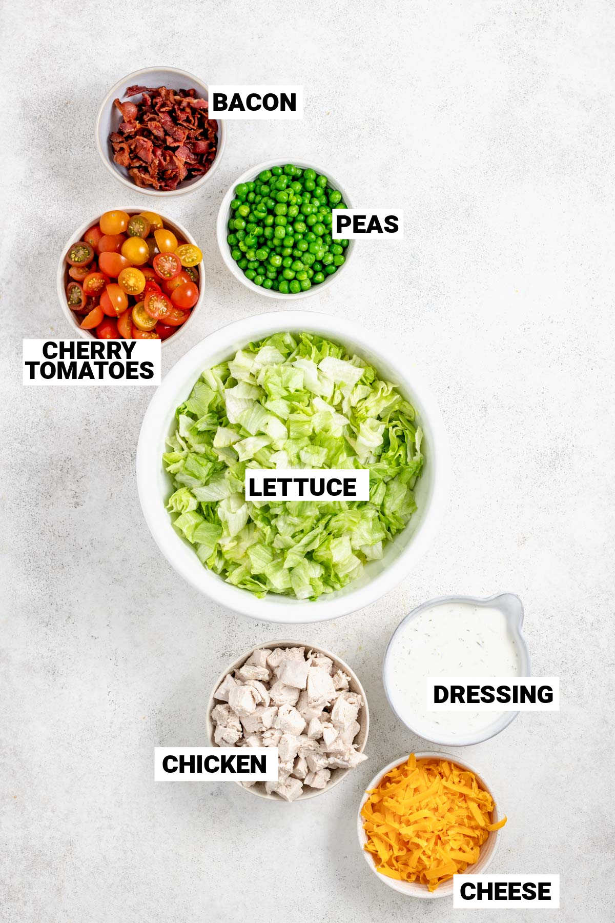 bacon, peas, cherry tomatoes, lettuce, chicken, creamy ranch dressing, and cheese set out in separate bowls
