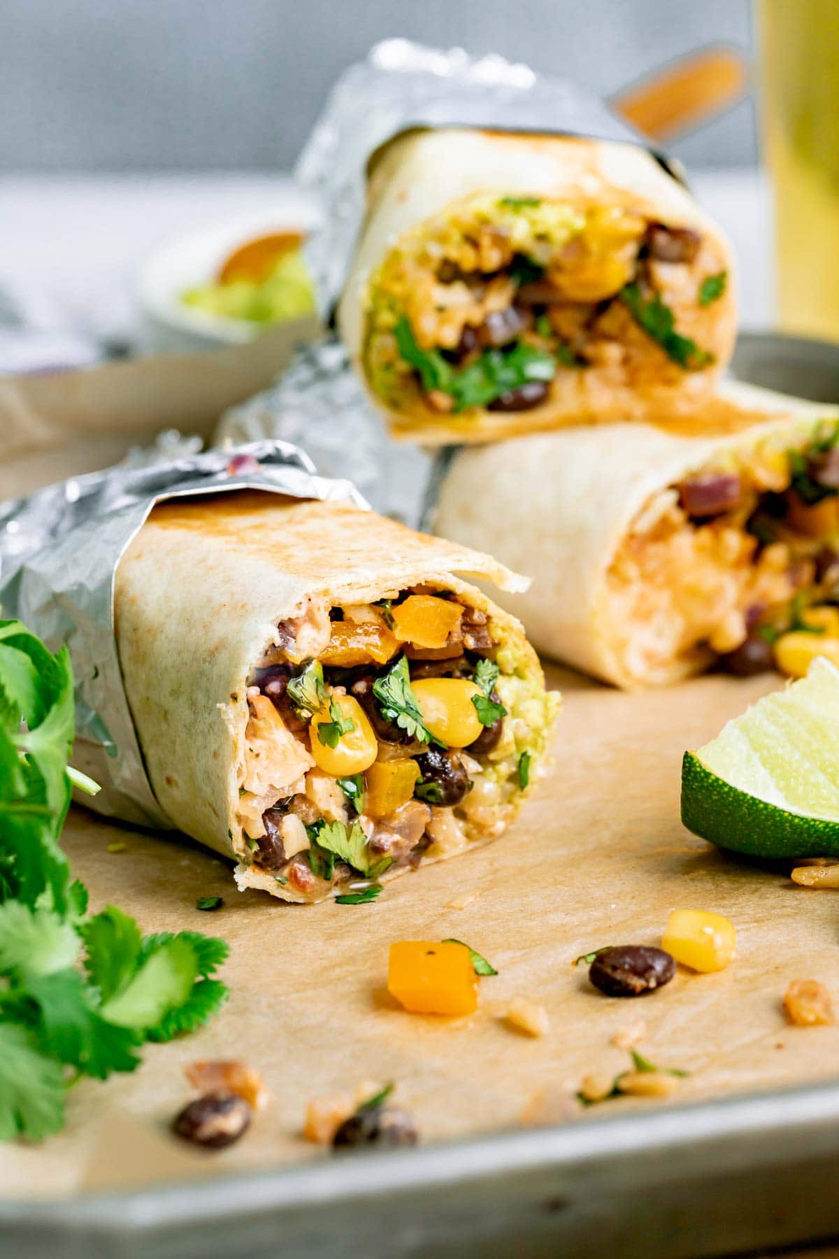 three foil wrapped veggie burritos on a parchment lined baking sheet