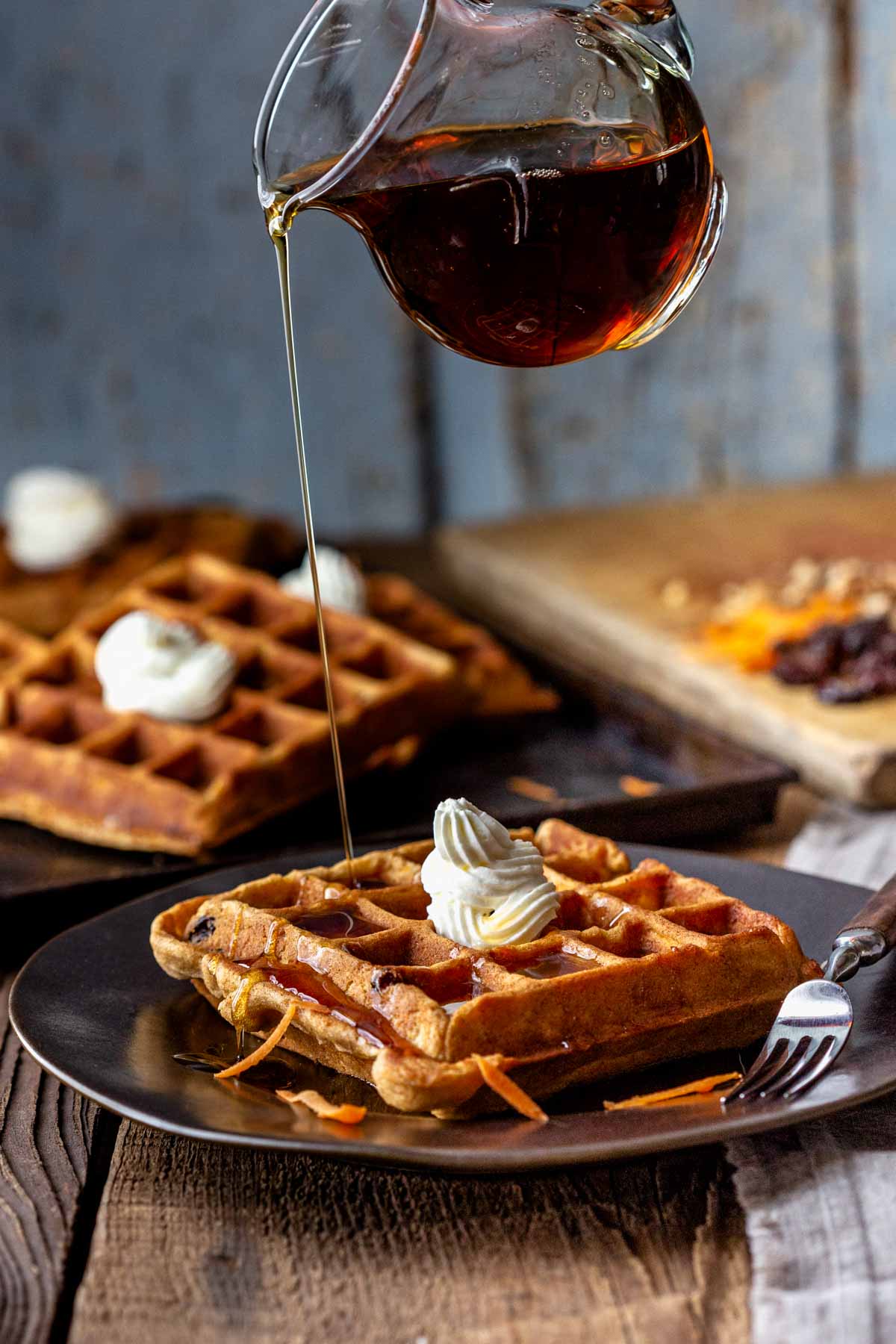 a pitcher of maple syrup drizzling over waffles with cream cheese